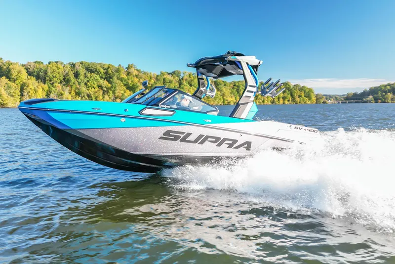 The Image of 2024 Supra SV 400 boat cruising on a lake with lush green shoreline. - 0