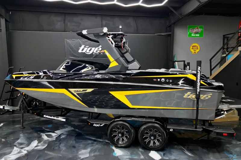 Slide: The Image of 2026 Tigé 22RZX boat in showroom, sleek black and yellow design on trailer. - 2