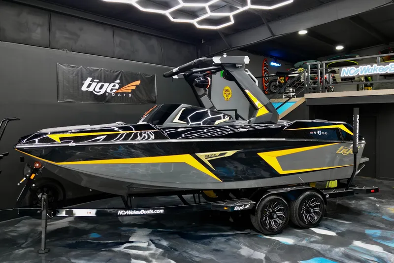 Slide: The Image of 2026 Tigé 22RZX boat in showroom, sleek black and yellow design, on trailer. - 24