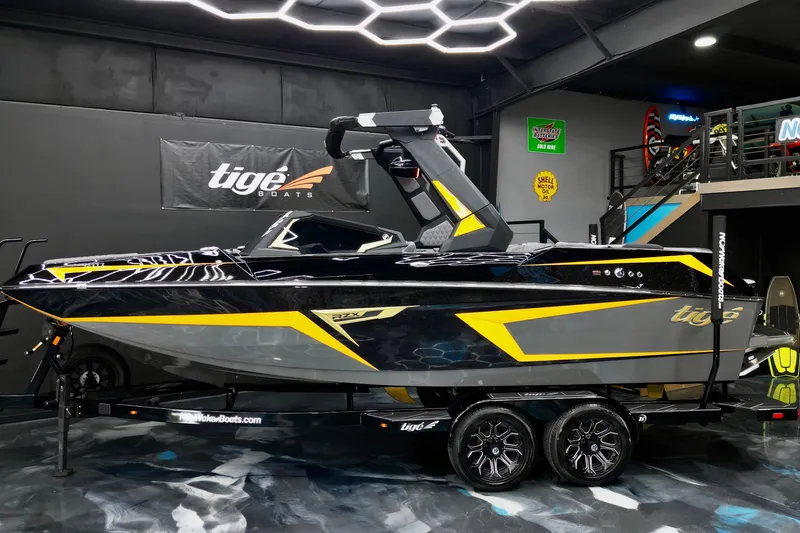Slide: The Image of 2026 Tigé 22RZX boat in showroom, sleek black and yellow design, on trailer. - 25