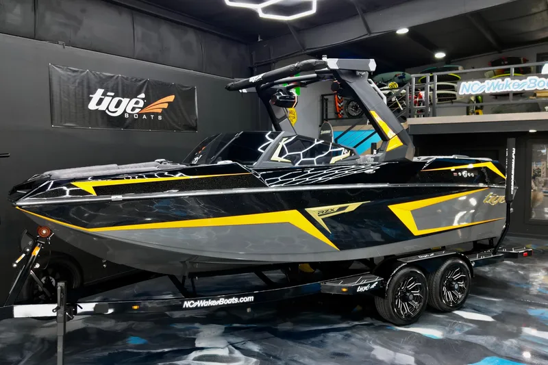Slide: The Image of 2026 Tigé 22RZX boat in showroom, sleek black and yellow design, on trailer. - 8