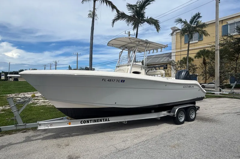 The Image of 2022 Cobia 237 Center Console boat on trailer, parked outdoors with palm trees. - 0
