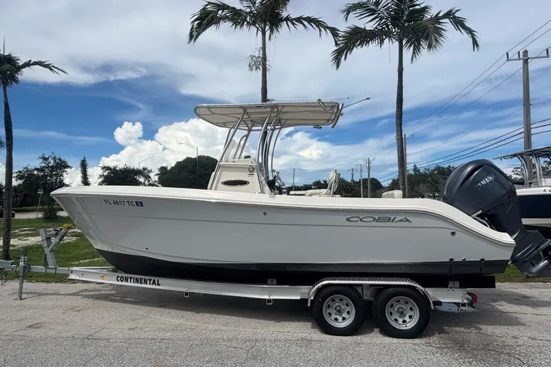 Slide: The Image of 2022 Cobia 237 Center Console boat on trailer, parked under palm trees. - 2