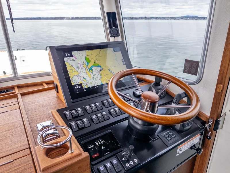 Slide: The Image of 2024 Targa 37 boat helm with navigation screen and wooden steering wheel on calm waters. - 12
