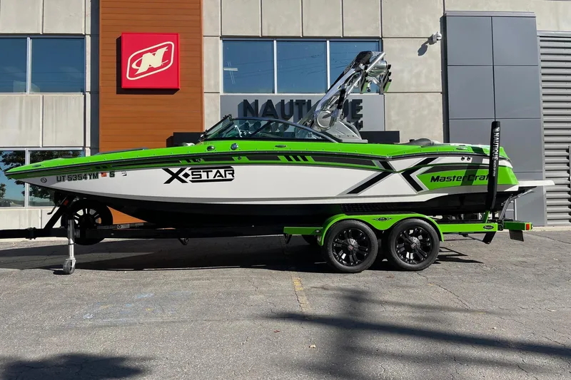 The Image of 2013 MasterCraft XStar boat in vibrant green and white, parked outside a Nautique dealership. - 1