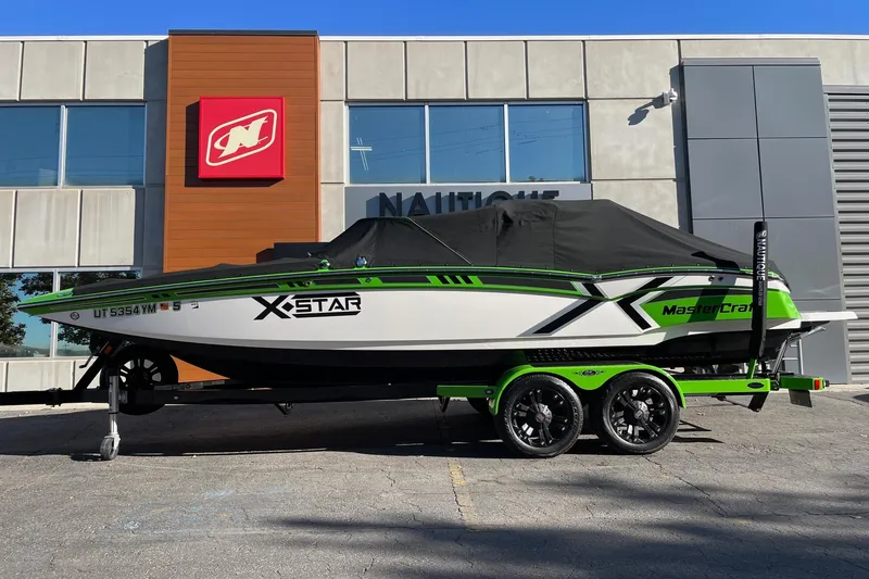 Slide: The Image of 2013 MasterCraft XStar boat with cover on green trailer, parked outside a building. - 15