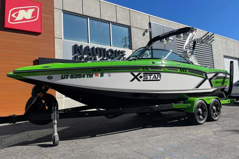 Slide: The Image of 2013 MasterCraft XStar boat with green accents on a trailer outside a dealership. - 2