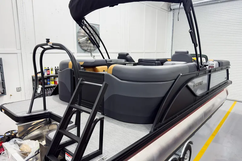 Slide: The Image of 2026 Godfrey Sweetwater 22' Split Bench Tritoon in a garage, showcasing sleek design and seating. - 5