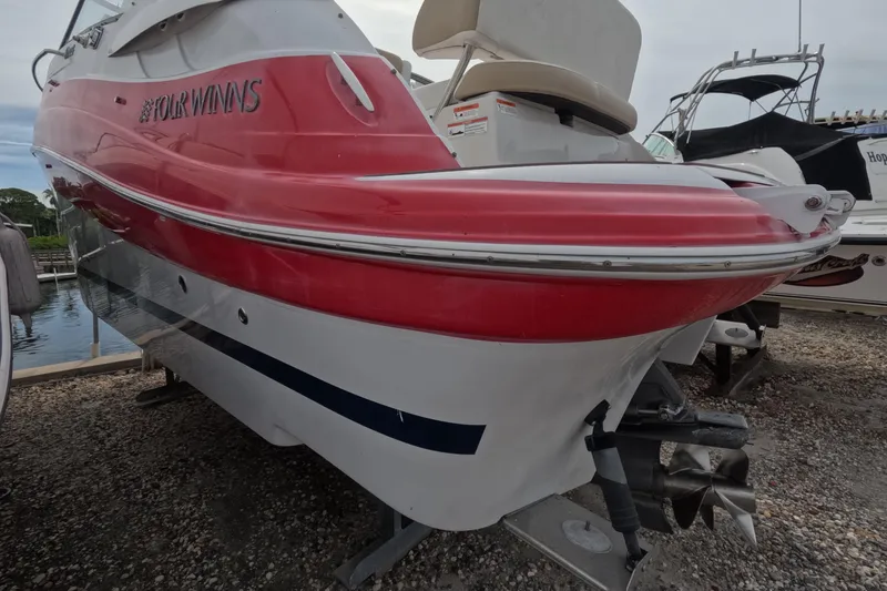 Slide: The Image of 2012 Four Winns V265 boat with red and white hull, docked on gravel. - 17