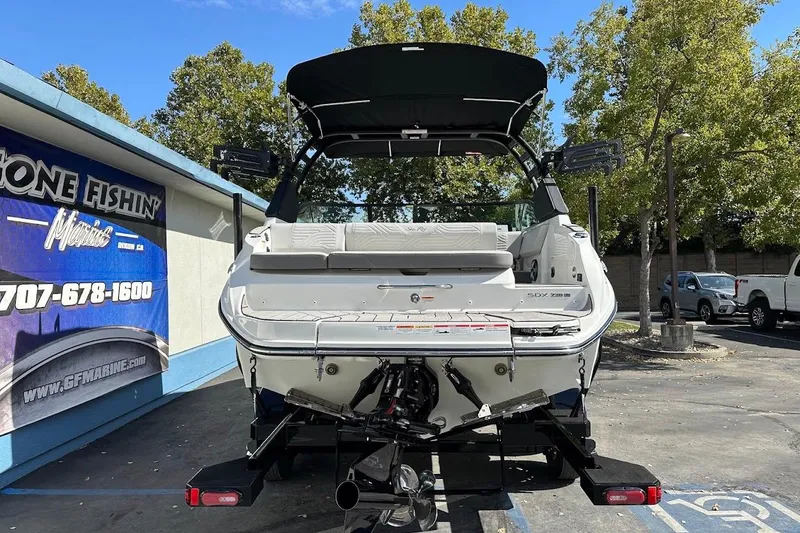 Slide: The Image of 2026 Sea Ray SDX 230 Surf boat displayed outdoors, rear view, with trees and signage. - 9