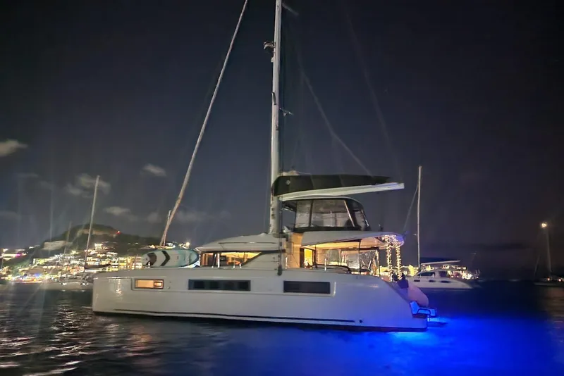 Slide: The Image of 2023 Lagoon 50 yacht illuminated at night, docked near a lit-up coastal town. - 4