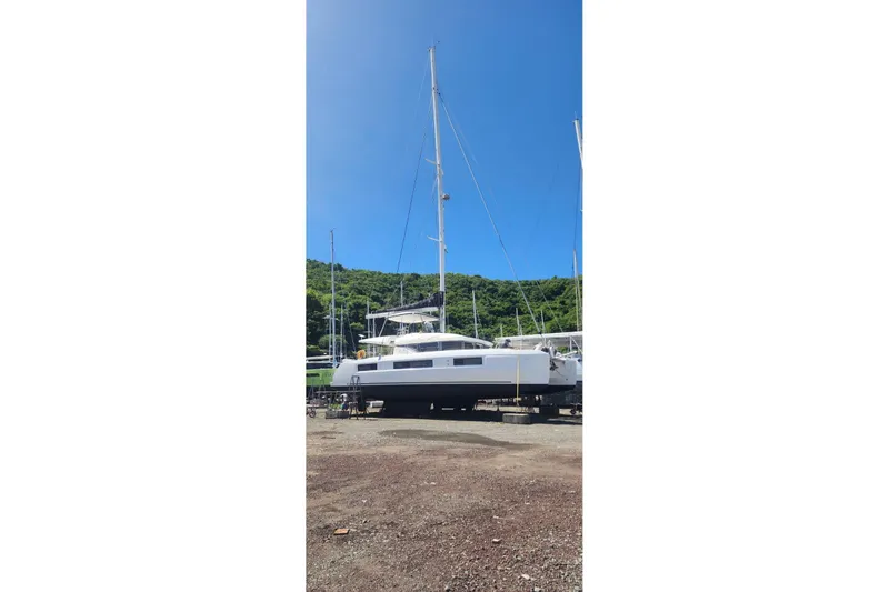 Slide: The Image of 2023 Lagoon 50 catamaran on land, clear sky, lush green background. - 84