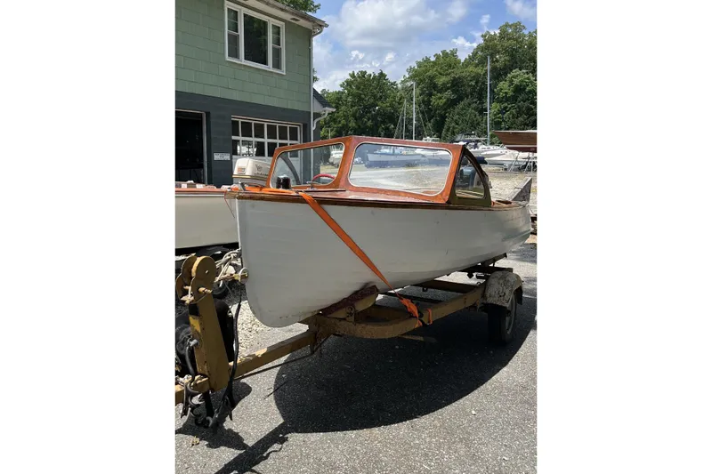 Slide: The Image of 1954 Lyman outboard boat on trailer, parked near a building and trees. - 0