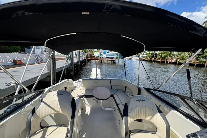 Slide: The Image of 2021 Stingray 231 DC boat interior with seating and canopy, docked by a scenic waterway. - 6