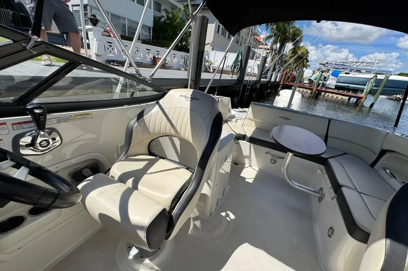 Slide: The Image of 2021 Stingray 231 DC boat interior with seating and steering wheel, docked by waterfront homes. - 7