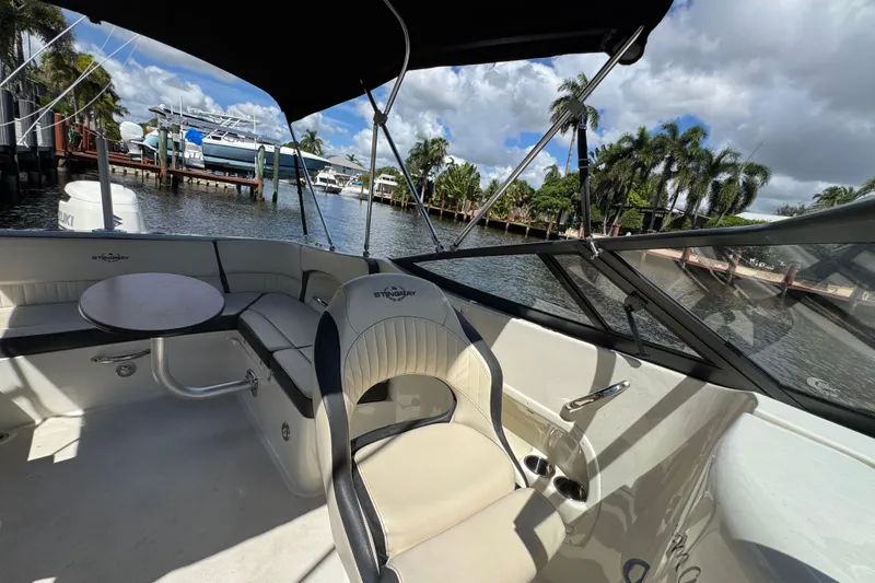 Slide: The Image of 2021 Stingray 231 DC boat interior with seating and table, docked by a scenic waterfront. - 9