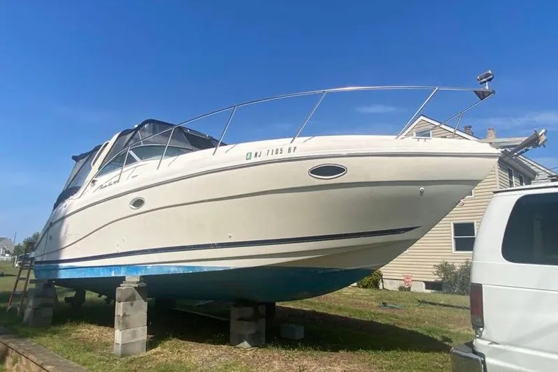 Slide: The Image of 2001 Rinker 310 Fiesta Vee boat on blocks, parked outdoors under clear blue sky. - 2