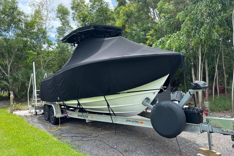 Slide: The Image of 2020 Blackfin 252 CC boat covered on trailer, surrounded by trees. - 33
