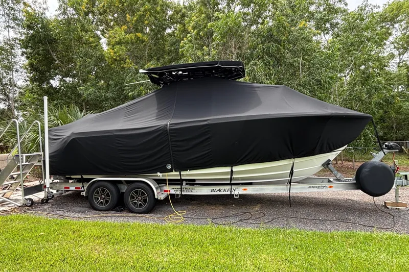 Slide: The Image of 2020 Blackfin 252 CC boat covered on trailer, surrounded by trees. - 34