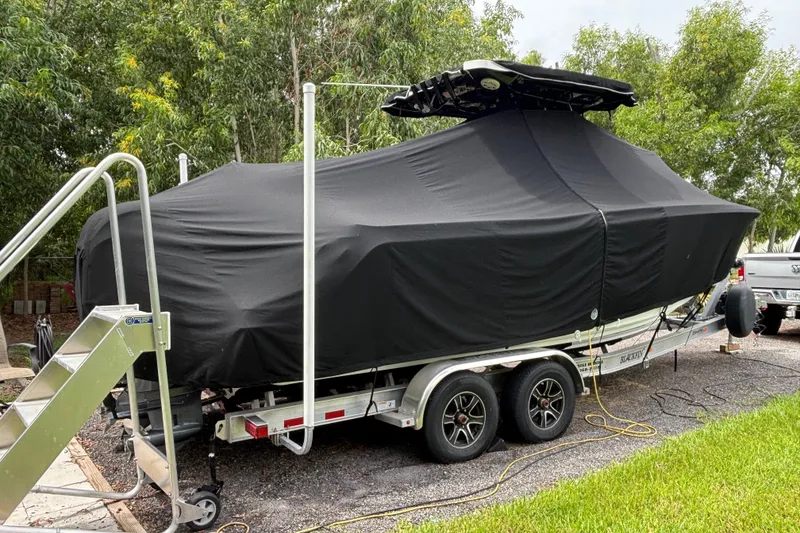 Slide: The Image of 2020 Blackfin 252 CC boat covered on trailer, parked outdoors near trees. - 35