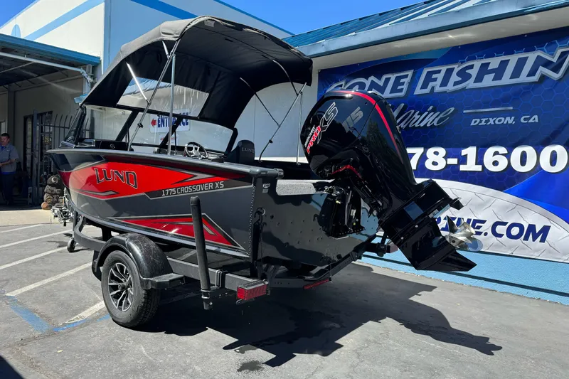 Slide: The Image of 2026 Lund 1775 Crossover XS boat with canopy, parked outside a marine store. - 5