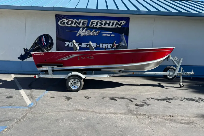 Slide: The Image of 2026 Lund 1600 Fury SS boat on trailer, red and silver, parked outside dealership. - 0