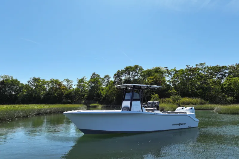Slide: The Image of 2026 NauticStar 252 Legacy boat on calm water with lush greenery background. - 13