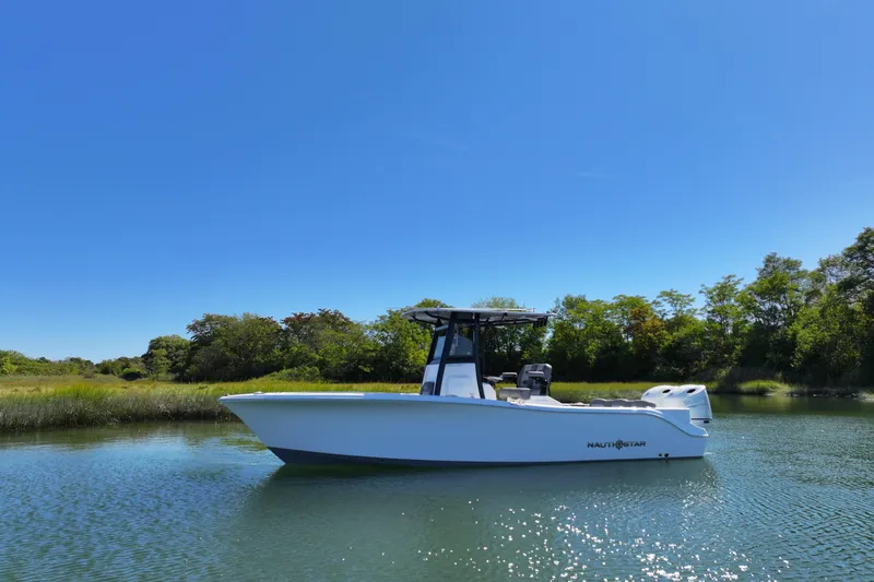 Slide: The Image of 2026 NauticStar 252 Legacy boat on calm water with lush greenery background. - 14