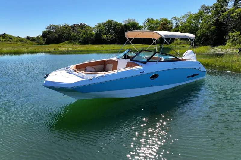 The Image of 2025 NauticStar 243 DC Deck boat on serene water with lush greenery background. - 1