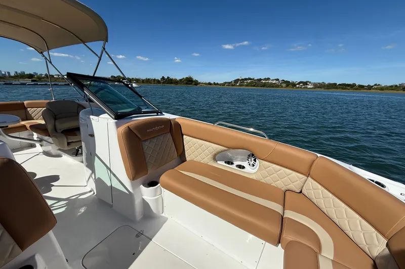 Slide: The Image of 2025 NauticStar 243 DC Deck boat with tan seating, cruising on a sunny lake. - 10