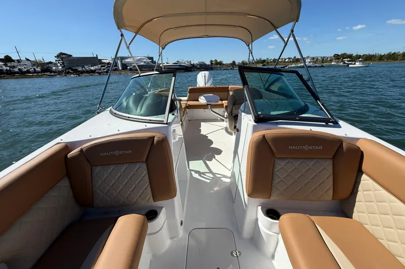 Slide: The Image of 2025 NauticStar 243 DC Deck boat with tan seating, cruising on a sunny day. - 11