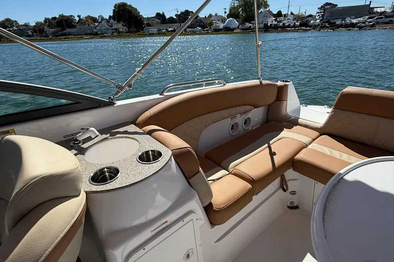 Slide: The Image of 2025 NauticStar 243 DC Deck boat interior with tan seating and cup holders on a sunny day. - 15