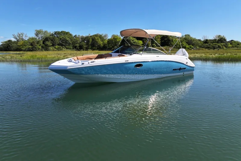 Slide: The Image of 2025 NauticStar 243 DC Deck boat on calm water, under clear blue sky. - 2