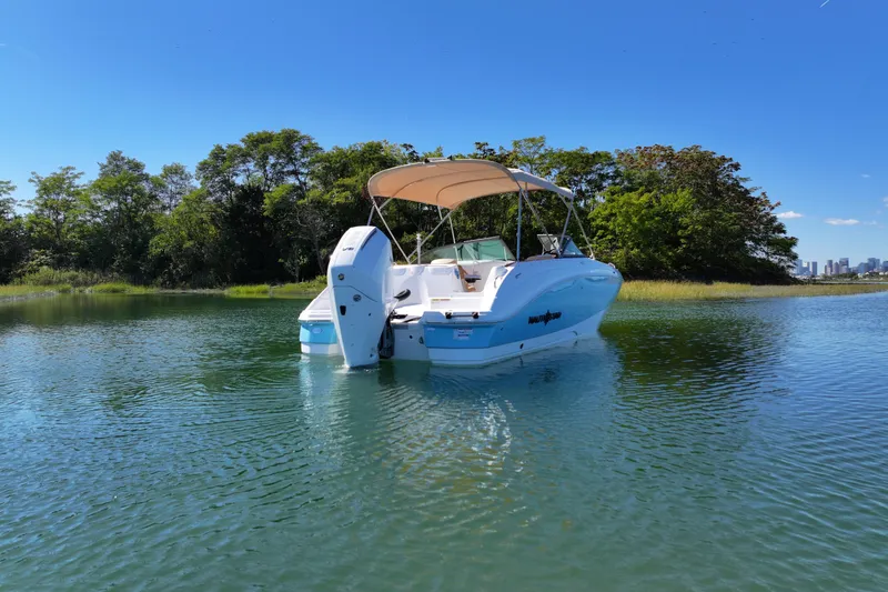 Slide: The Image of 2025 NauticStar 243 DC Deck boat on serene water, surrounded by lush greenery. - 5