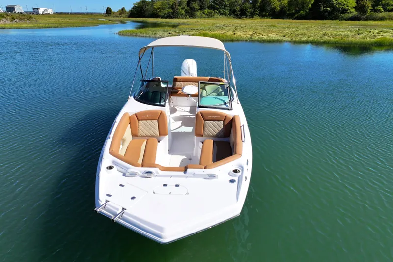 Slide: The Image of 2025 NauticStar 243 DC Deck boat on serene water, featuring tan seating and canopy. - 7