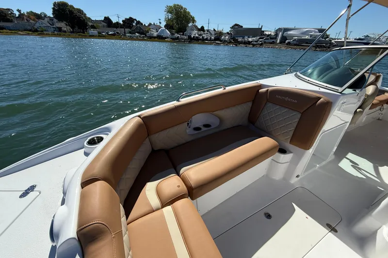 Slide: The Image of 2025 NauticStar 243 DC Deck boat with tan seating on a sunny day by the water. - 9