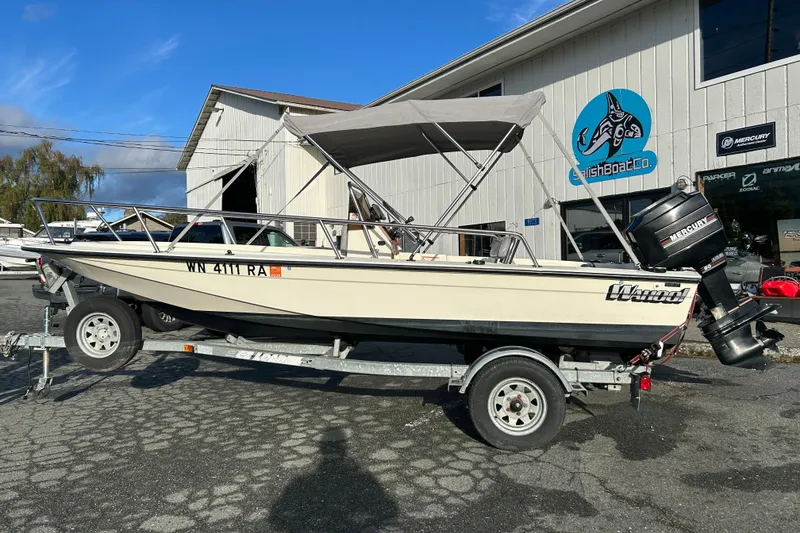 The Image of 1990 Wahoo 16.2 Striper boat on trailer, parked outside a marine shop. - 0