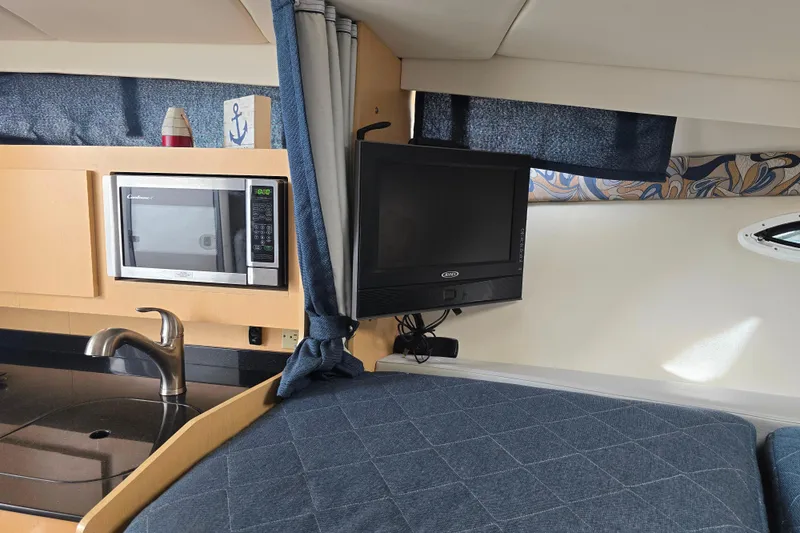 Slide: The Image of 2011 Bayliner 285 interior with microwave, TV, and sink in cozy cabin setting. - 16