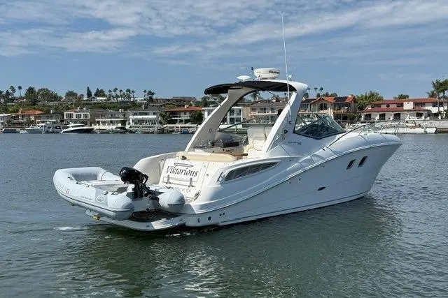 Slide: The Image of 2012 Sea Ray 330 Sundancer yacht on calm water, with coastal homes in the background. - 2