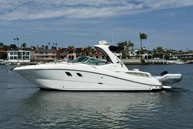 Slide: The Image of 2012 Sea Ray 330 Sundancer yacht on calm water, with coastal homes in the background. - 4
