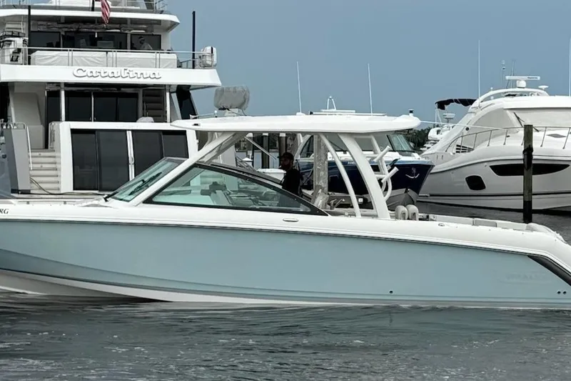 Slide: The Image of 2017 Boston Whaler 320 Vantage boat docked near luxury yachts in a marina. - 1