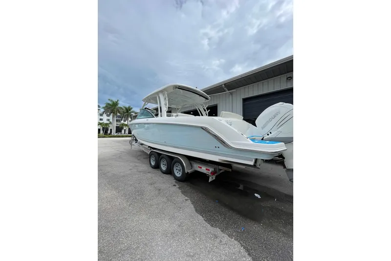 Slide: The Image of 2017 Boston Whaler 320 Vantage boat on trailer, parked near a building under cloudy sky. - 33