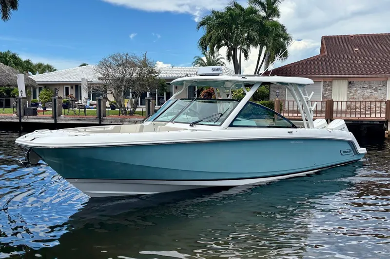The Image of 2024 Boston Whaler 320 Vantage boat docked near waterfront homes, under a clear sky. - 0