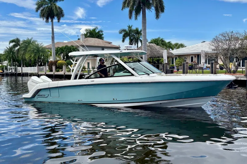 Slide: The Image of 2024 Boston Whaler 320 Vantage boat on calm water, surrounded by palm trees and waterfront homes. - 1