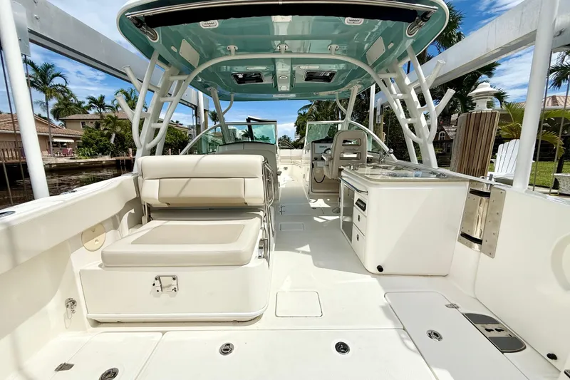 Slide: The Image of 2024 Boston Whaler 320 Vantage boat interior with seating and helm, docked near palm trees. - 11