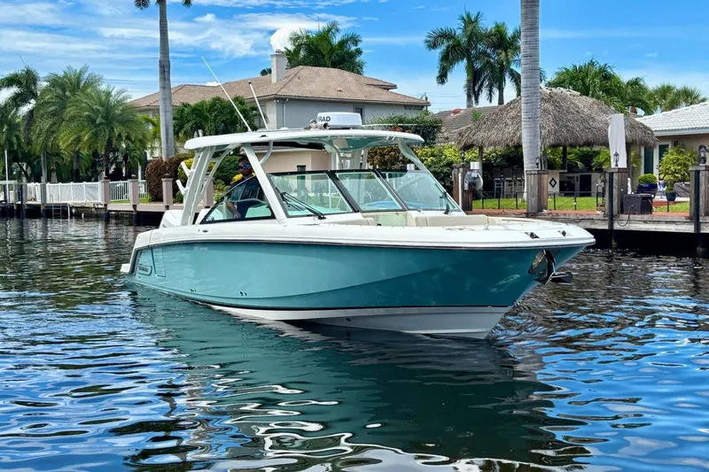 Slide: The Image of 2024 Boston Whaler 320 Vantage boat on a scenic waterfront with palm trees. - 6