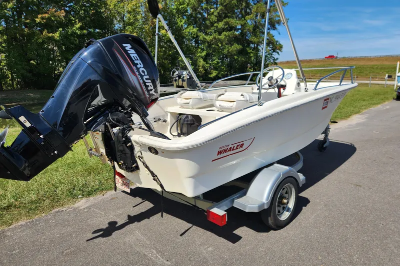 Slide: The Image of 2018 Boston Whaler 130 Super Sport boat on trailer with Mercury engine, parked outdoors. - 2
