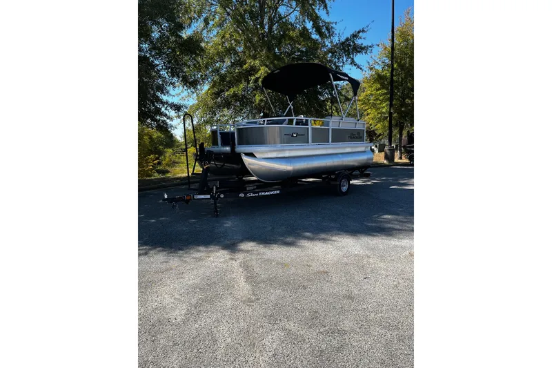 The Image of 2026 Sun Tracker Bass Buggy 16 XL Select pontoon boat on trailer, parked outdoors. - 0