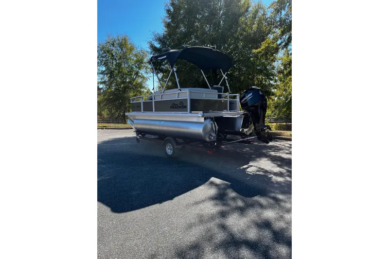 Slide: The Image of 2026 Sun Tracker Bass Buggy 16 XL Select pontoon boat on trailer, parked outdoors. - 2