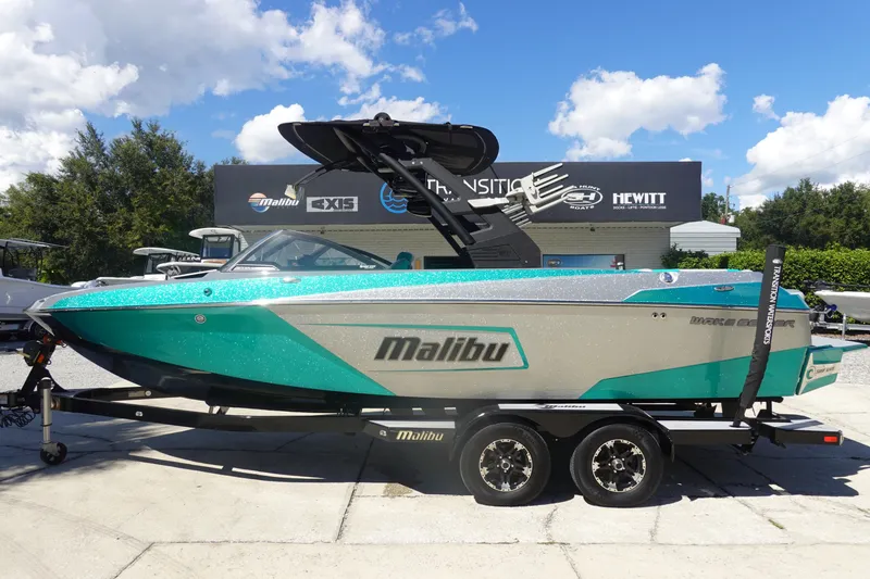 The Image of 2019 Malibu Wakesetter 23 LSV boat on trailer, teal and gray design, parked outdoors. - 1